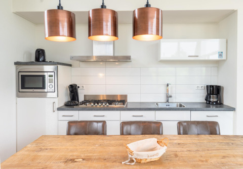 Moderne keuken in Cube Exclusif 4 lodge te Schoneveld, Nederland, met houten tafel en koperen lampen.