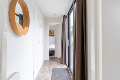 Heldere gang in Cube Exclusif 4 lodge te Schoneveld, Nederland, met grote ramen en houten spiegel.