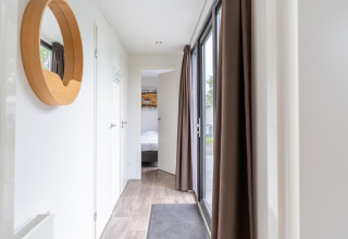 Heldere gang in Cube Exclusif 4 lodge te Schoneveld, Nederland, met grote ramen en houten spiegel.