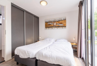 Dormitorio luminoso con dos camas individuales, arte moderno y ventanas grandes en Cube Exclusif 4, Schoneveld, Países Bajos.