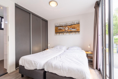 Dormitorio luminoso con dos camas individuales, arte moderno y ventanas grandes en Cube Exclusif 4, Schoneveld, Países Bajos.