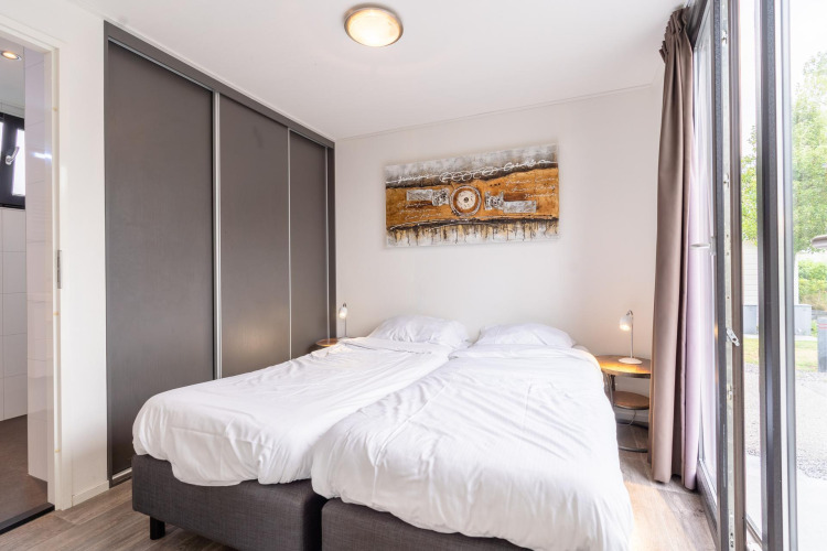 Dormitorio luminoso con dos camas individuales, arte moderno y ventanas grandes en Cube Exclusif 4, Schoneveld, Países Bajos.