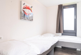 Helles Schlafzimmer im Cube Exclusif 4 mit zwei Betten, großem Fenster und moderner Kunst in Schoneveld, Niederlande.