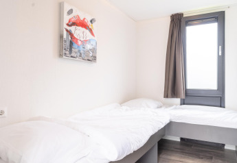 Helles Schlafzimmer im Cube Exclusif 4 mit zwei Betten, großem Fenster und moderner Kunst in Schoneveld, Niederlande.