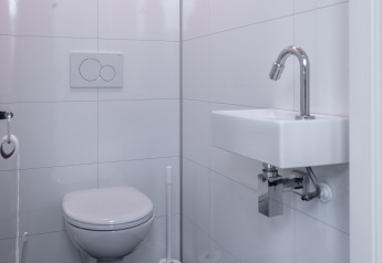 Moderne witte badkamer met zwevend toilet en kleine lavabo in Cube Exclusif 4, Schoneveld, Nederland.