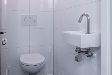 Moderne witte badkamer met zwevend toilet en kleine lavabo in Cube Exclusif 4, Schoneveld, Nederland.