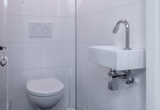 Moderno baño blanco con inodoro de pared y lavabo pequeño en Cube Exclusif 4, Schoneveld, Países Bajos.