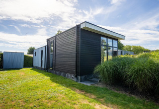 Modern Cube Exclusif 4 lodge at Schoneveld in the Netherlands, featuring black wood paneling and large windows.