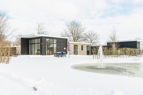 Moderne Lodge mit großen Fenstern, verschneite Landschaft und Teich im Vakantiepark Hölte, Niederlande.