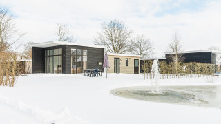 Lodge moderne aux grandes baies vitrées, neige et fontaine au Vakantiepark Hölte, Pays-Bas.