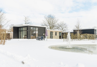 Moderne lodge met grote ramen, sneeuwlandschap en fontein bij Vakantiepark Hölte, Nederland.