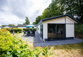 Familie nyder udendørs siddepladser ved Comfort-hytte i EuroParcs Noordwijkse Duinen, Holland.