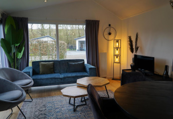 Moderne stue i Comfort-hytte på EuroParcs Noordwijkse Duinen med blå sofa og store vinduer.