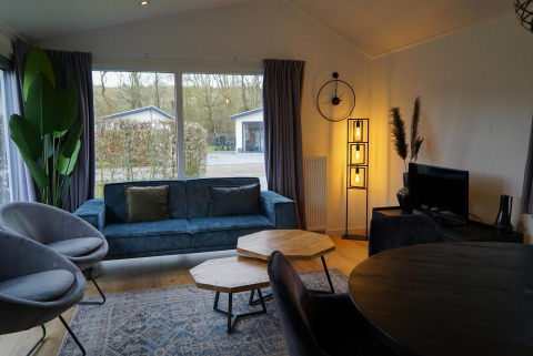 Moderne stue i Comfort-hytte på EuroParcs Noordwijkse Duinen med blå sofa og store vinduer.