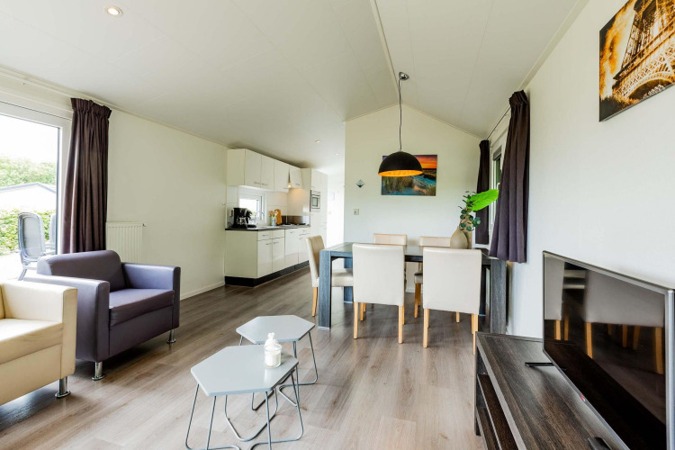 Salón y cocina en una cabaña Comfort en EuroParcs Noordwijkse Duinen, decoración moderna, mesa y televisor.