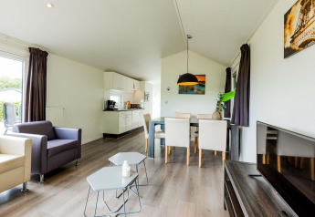 Salón y cocina en una cabaña Comfort en EuroParcs Noordwijkse Duinen, decoración moderna, mesa y televisor.