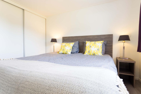 Slaapkamer met tweepersoonsbed, gele kussens, moderne lampen en kast in Comfort hut bij EuroParcs Noordwijkse Duinen.