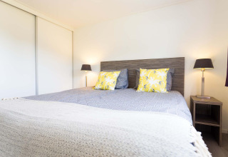 Dormitorio con cama doble, cojines amarillos, lámparas modernas y armario en la cabaña Comfort de EuroParcs Noordwijkse Duinen.