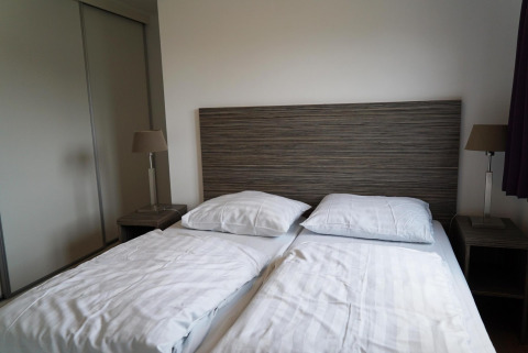 Modern tweepersoonsbed met houten hoofdbord, nachtkastjes en lampen in Comfort cabin bij EuroParcs Noordwijkse Duinen.