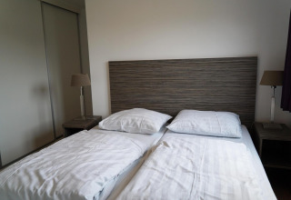 Modern tweepersoonsbed met houten hoofdbord, nachtkastjes en lampen in Comfort cabin bij EuroParcs Noordwijkse Duinen.