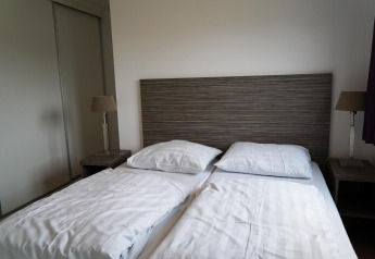 Moderna cama doble con cabecero de madera, mesitas y lámparas en la cabaña Comfort de EuroParcs Noordwijkse Duinen.