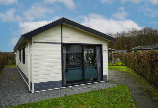 Buitenaanzicht van Comfort-hut bij EuroParcs Noordwijkse Duinen in Nederland, met hagen en paadje.