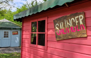 To små hytter med skilte 'SALINGER' og 'KEROUAC' ved Writers Hut på Zomerlicht, Holland, omgivet af træer.