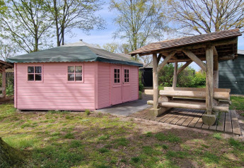 Cabane d’écrivain rose avec toit vert et banc abrité en bois, jardin de Zomerlicht, Pays-Bas, printemps.