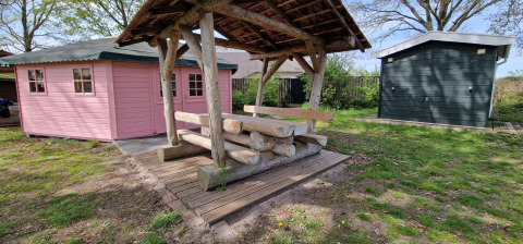 Outdoor photo of a small pink wooden hut and rustic bench under shelter at Writers hut, Zomerlicht, Netherlands.