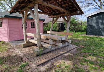 Photo extérieure d’une petite cabane rose et d’un banc rustique sous abri au Writers hut, Zomerlicht, Pays-Bas.