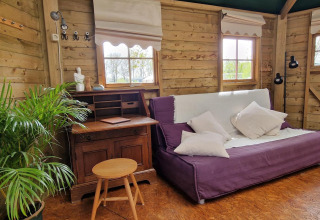 Acogedora sala en Writers hut en Zomerlicht, Países Bajos, con sofá, escritorio, planta y paredes de madera.