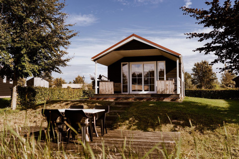 Træhytte med overdækket terrasse og udendørs spiseområde i naturskønne omgivelser ved glamping.