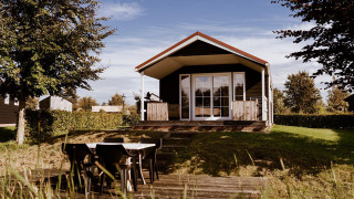 Træhytte med overdækket terrasse og udendørs spiseområde i naturskønne omgivelser ved glamping.