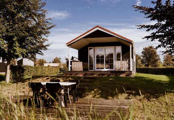 Cabaña de madera con porche cubierto y comedor exterior en un entorno natural ideal para glamping.