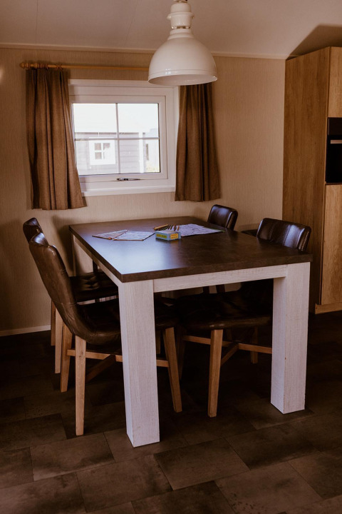 Mesa de comedor con cuatro sillas en un lodge, lámpara colgante y ventana con cortinas marrones.