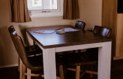 Mesa de comedor con cuatro sillas en un lodge, lámpara colgante y ventana con cortinas marrones.