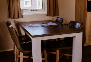 Table à manger avec quatre chaises dans un lodge, fenêtre équipée de rideaux marron et suspension.