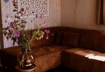 Angolo accogliente di un lodge con divano marrone, fiori selvatici in vaso di vetro e decorazione murale.