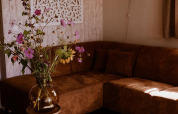 Gezellige lodge-hoek met bruine hoekbank, veldbloemen in glazen vaas en decoratief muurkunstwerk.