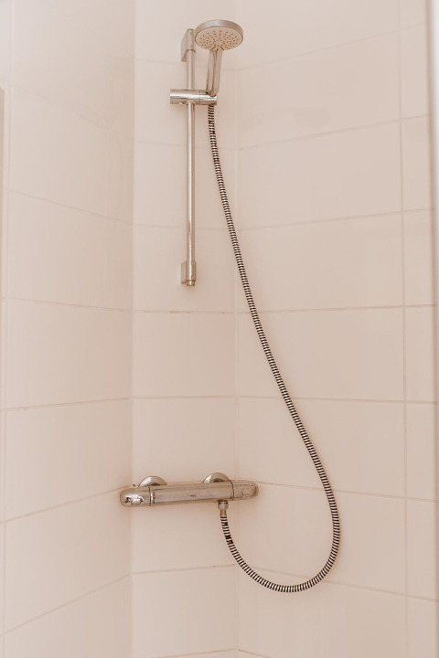 Ducha moderna con rociador de mano y grifo mezclador, instalada sobre azulejos claros en una cabaña.