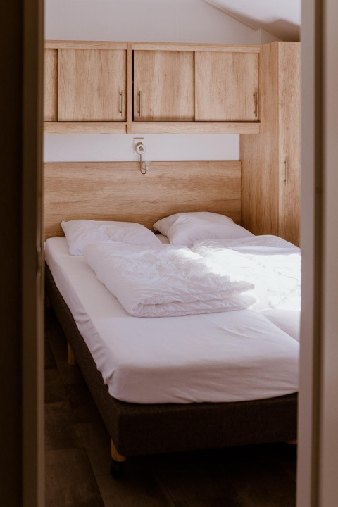 Narrow lodge bedroom with two single beds pushed together, white bedding, and wooden cabinets above.