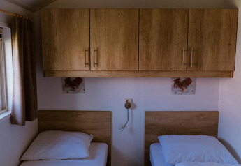 Deux lits simples sous des placards en bois dans une chambre de lodge, près d'une fenêtre à rideaux.