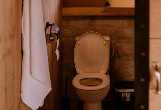 Salle de bain de tente safari avec toilettes, sol en bois, serviette blanche et fenêtre en arrière-plan.