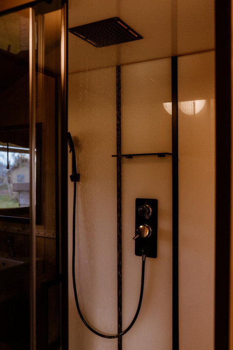 Modern shower inside a safari tent with a rainfall showerhead and handheld sprayer against bright walls.