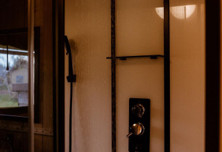 Modern shower inside a safari tent with a rainfall showerhead and handheld sprayer against bright walls.