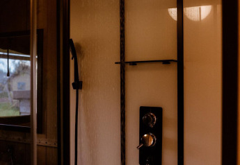 Modern shower inside a safari tent with a rainfall showerhead and handheld sprayer against bright walls.