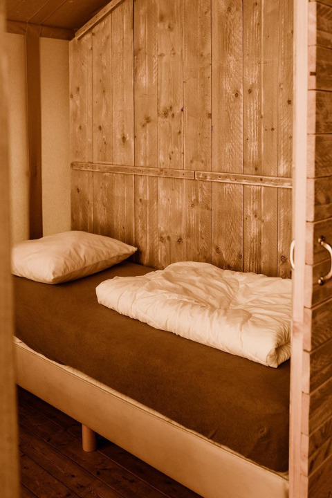 Gemütliches Bett mit Holzwänden in einem Safari-Glampingzelt im Ferienpark Eigen Wijze, Niederlande.