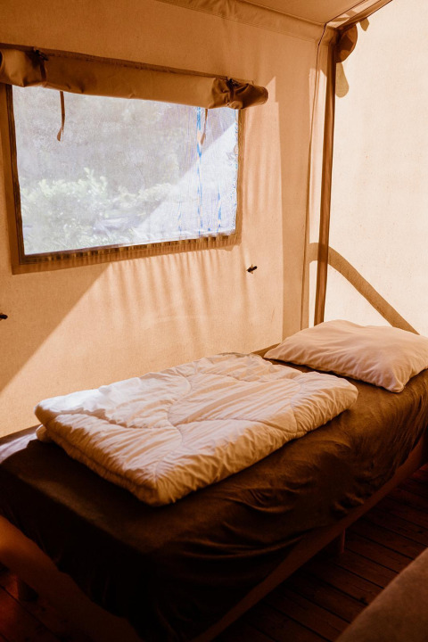 Cama individual con sábanas blancas en una tienda de glamping en Holiday park Eigen Wijze, Países Bajos.