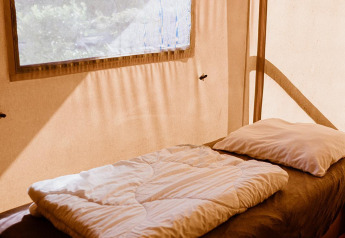 Letto singolo con biancheria bianca in una tenda glamping al Holiday park Eigen Wijze, Paesi Bassi.