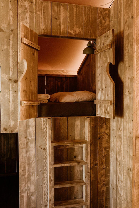 Holzbett mit Leiter in komfortablem Glamping-Zelt im Ferienpark Eigen Wijze, Niederlande.